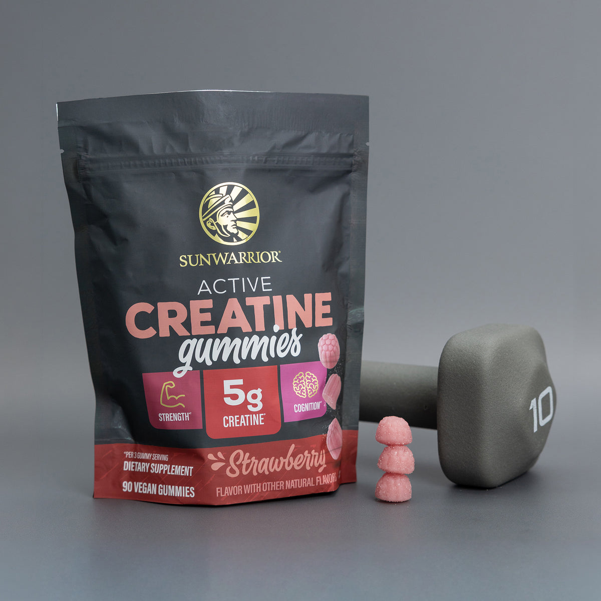 Sunwarrior strawberry creatine gummies package with gummies stacked next to a gray 10-pound dumbbell