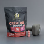 Sunwarrior strawberry creatine gummies package with gummies stacked next to a gray 10-pound dumbbell